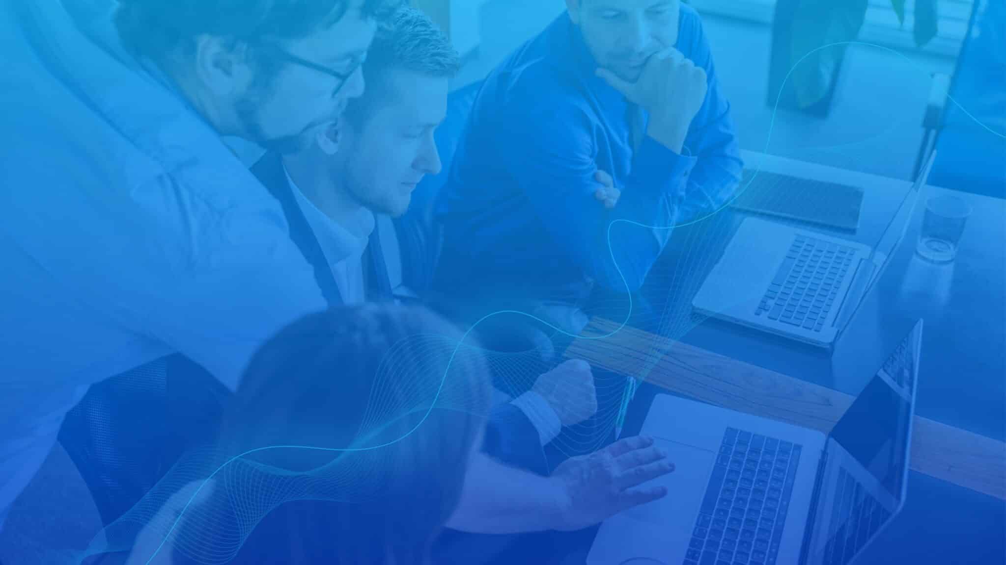 Business team collaborating on laptops, representing a strong cybersecurity program, adherence to relevant regulations, and improved security posture.